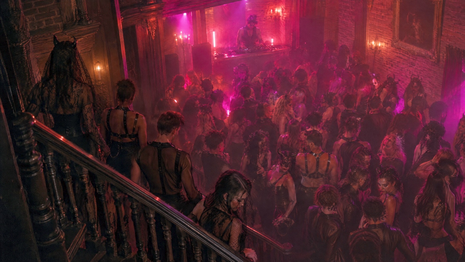 From a dark stair landing, a packed dance floor below glows red and magenta through the haze